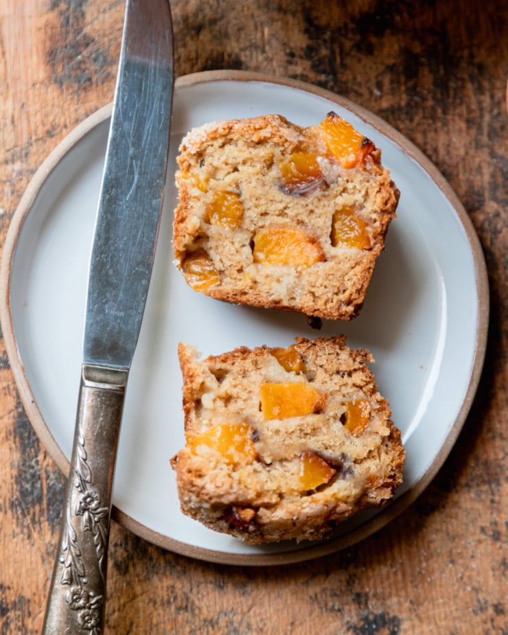 An overhead shot shows a peach muffin split in half on a plate with an antique silver knife nearby.
