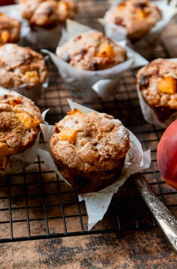 A 3/4 angle shot shows vegan peaches and cream muffins cooling in a wire rack against a rough wood board.