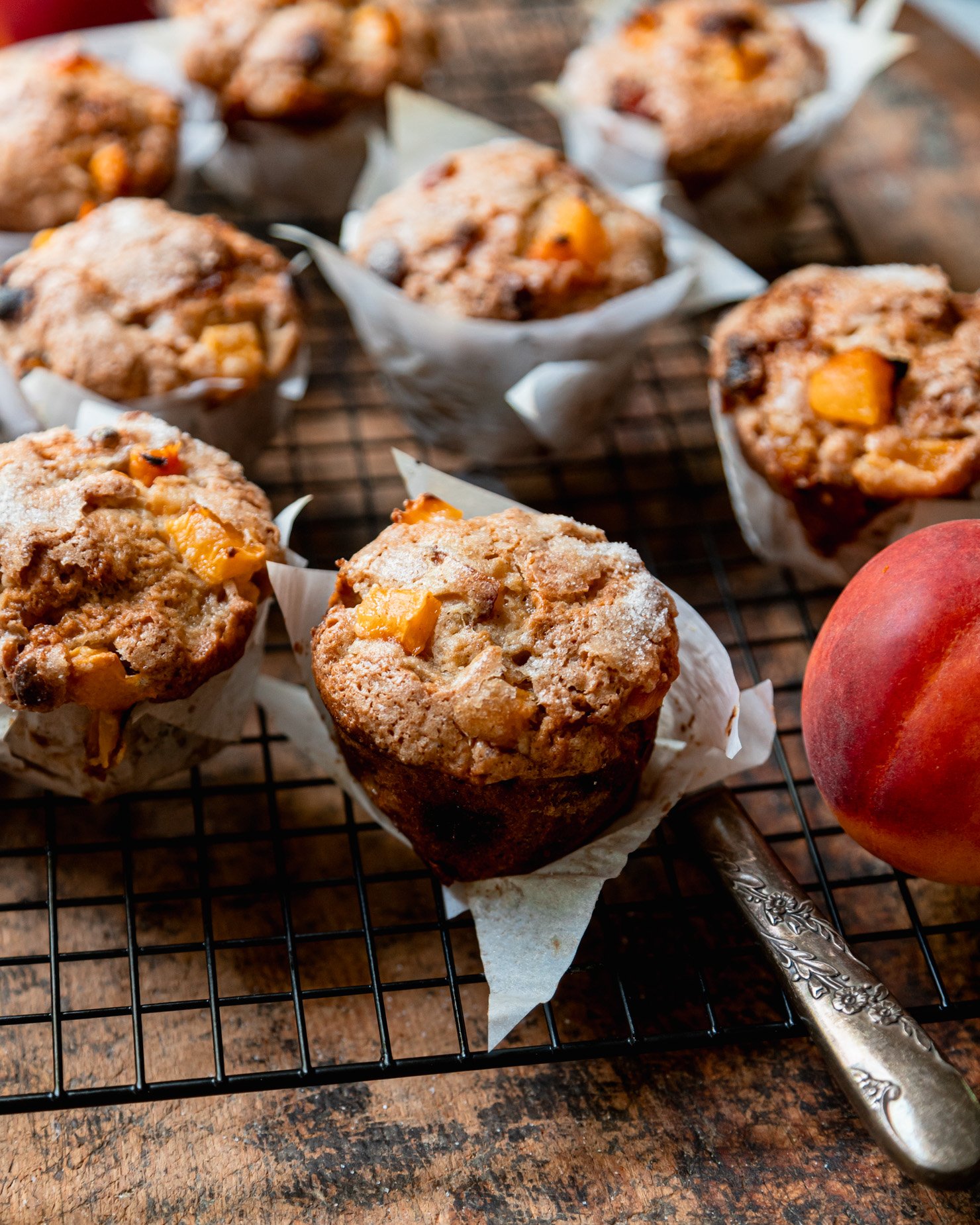 A 3/4 angle shot shows vegan peaches and cream muffins cooling in a wire rack against a rough wood board.