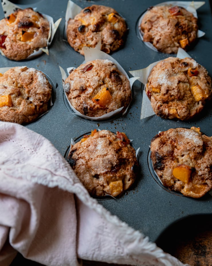 A 3/4 angle shot shows baked vegan peaches and cream muffins in a muffin tin.