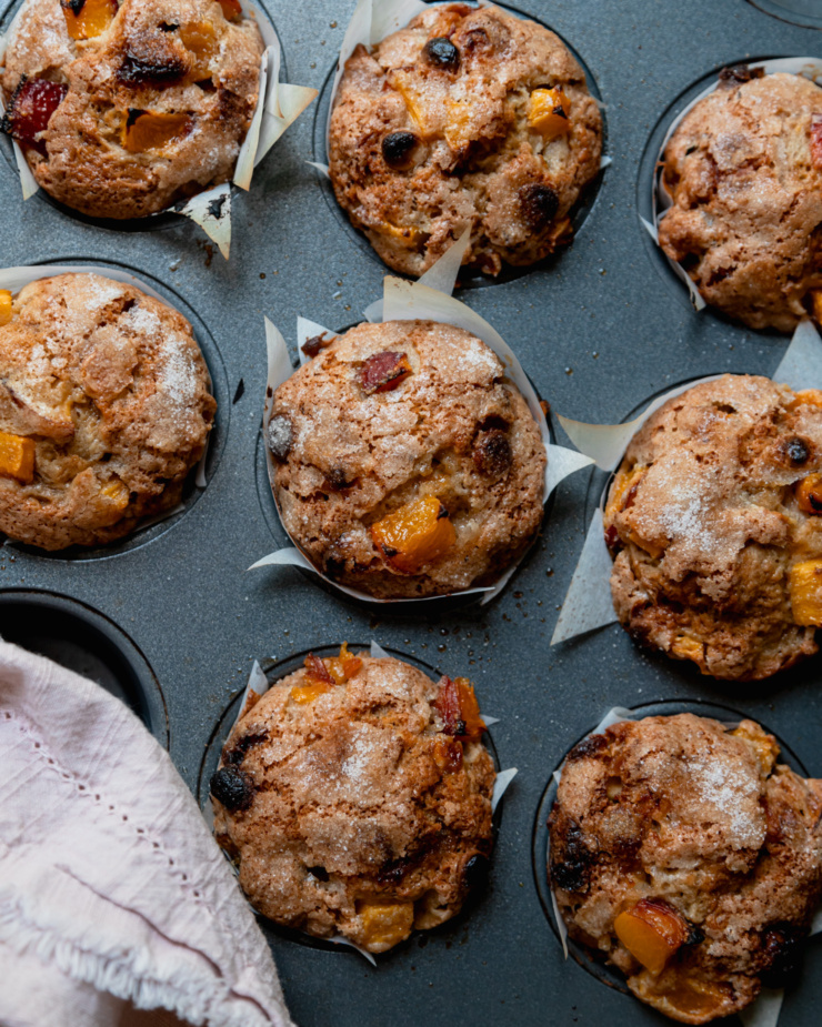 An overhead shot shows baked vegan peaches and cream muffins in a muffin tin.