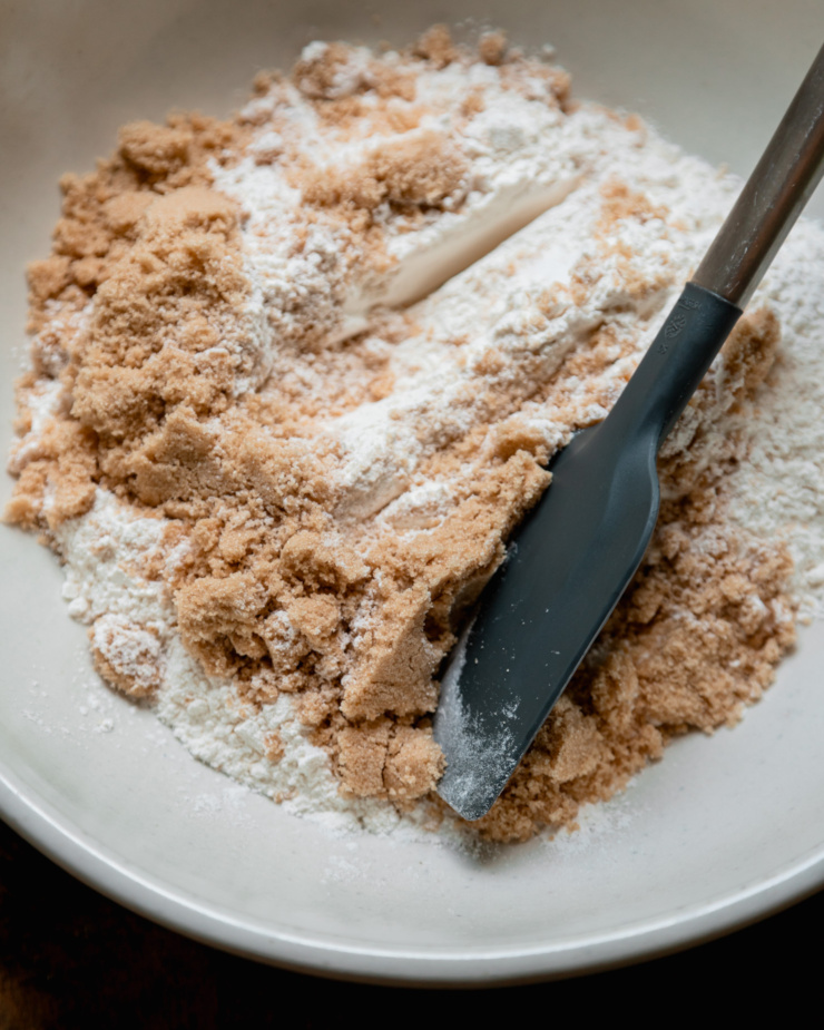 An overhead shot shows a bowl with flour and light brown sugar in it. A spatula is perched on top.
