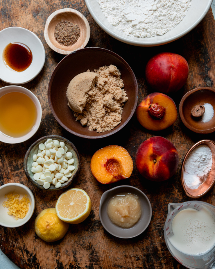 An overhead shot shows ingredients for a muffin recipe featuring fresh peaches and vegan white chocolate chips.