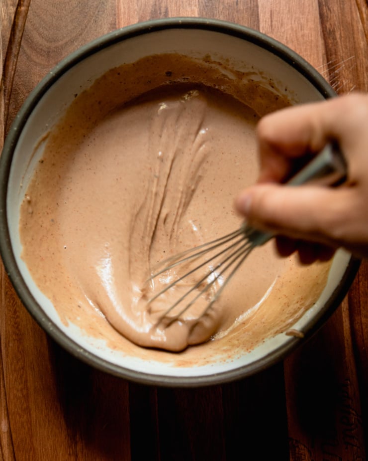 An overhead shot shows a hand whisking up some barbecue tahini ranch dressing in a bowl.