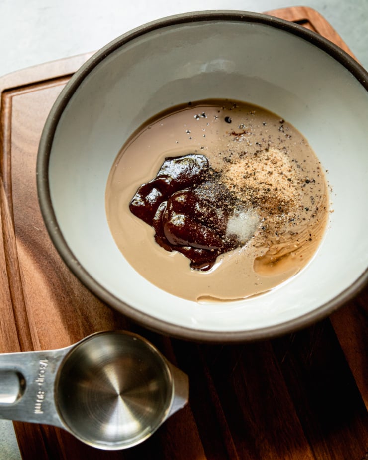 A 3/4 angle image shows a bowl with tahini, spices, barbecue sauce, salt, and pepper. A measuring cup with water is nearby.