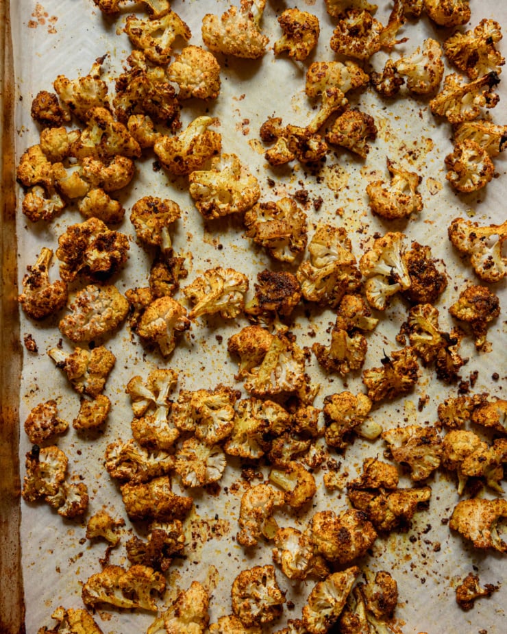 An overhead shot shows a baking sheet filled with golden, well-spiced roasted cauliflower.
