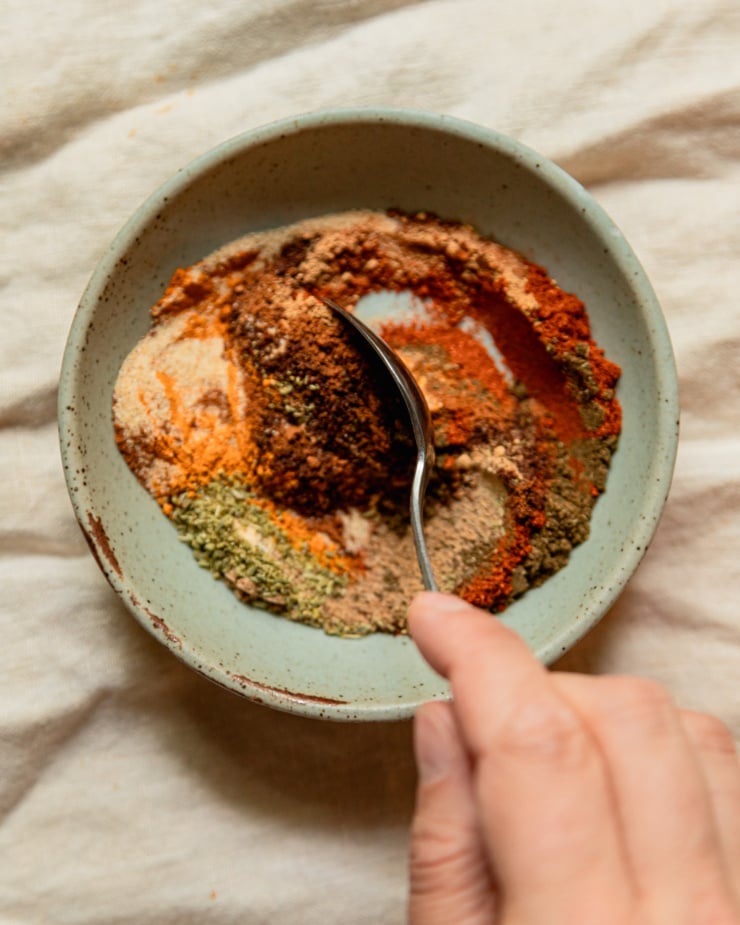 An overhead shot shows a hand stirring some spices together in a bowl.