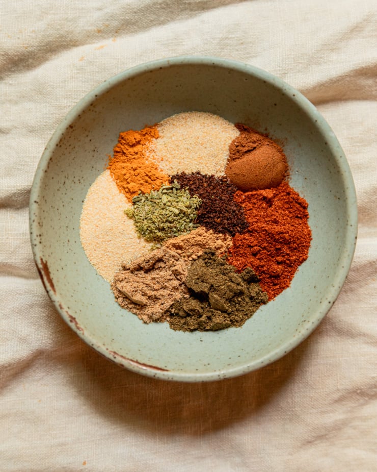 An overhead shot shows 10 different spices all measured out in segments in a small, shallow bowl.