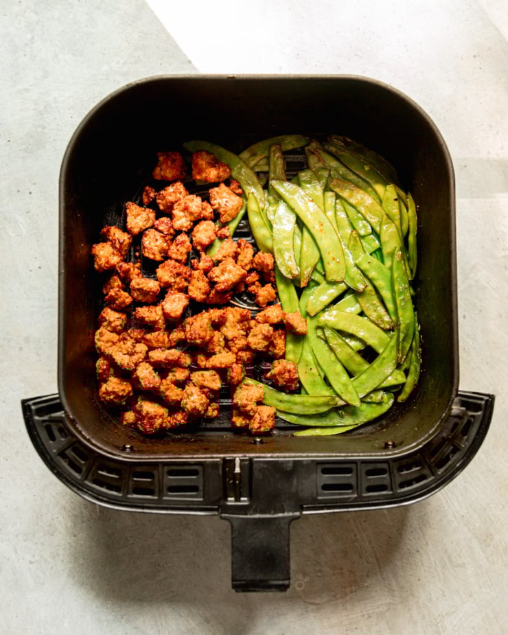 An overhead shot shows an air fryer basket filled with crispy tempeh bits and cooked snow peas.