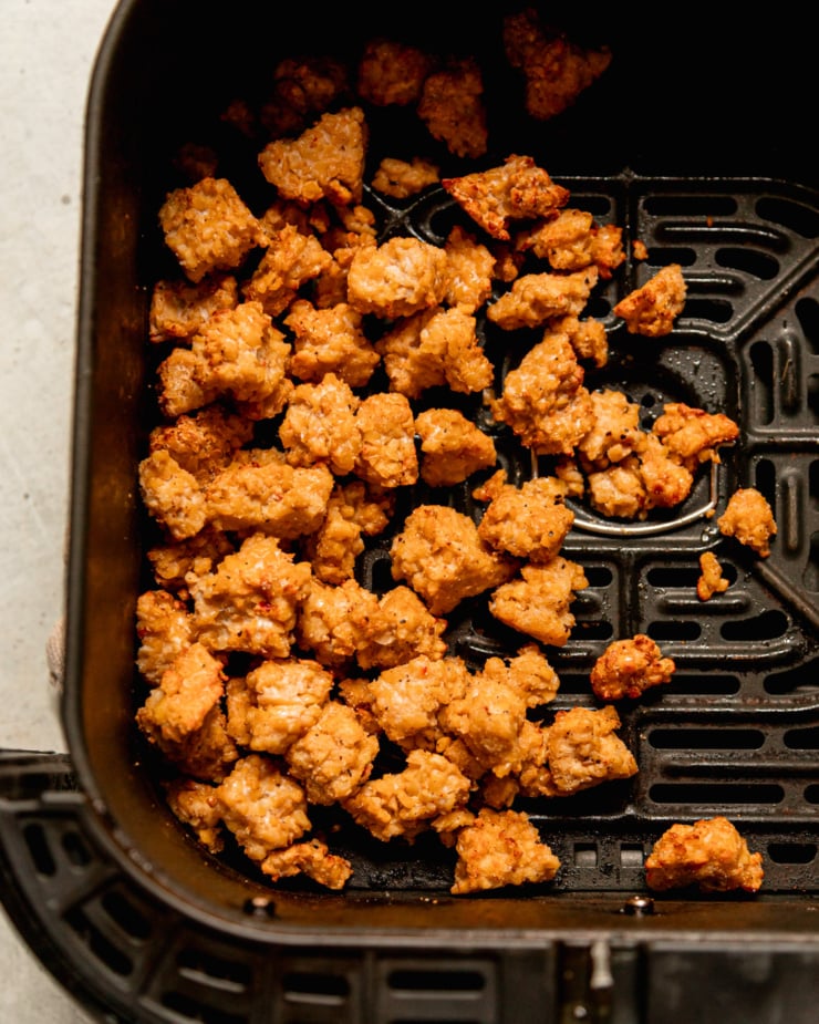 An overhead shot shows cooked tempeh bits in an air fryer basket.
