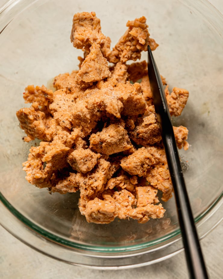 An overhead shot shows a bowl filled with torn tempeh pieces that have been dusted with spices.