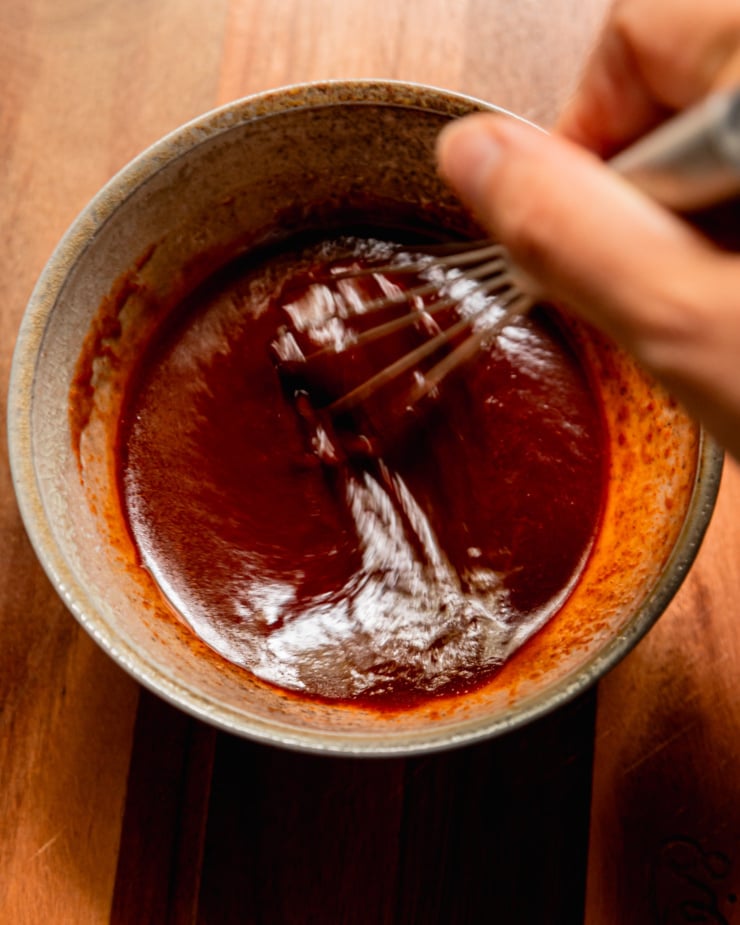An overhead shot shows a hand using a whisk to bring a gochujang glaze together in a bowl.