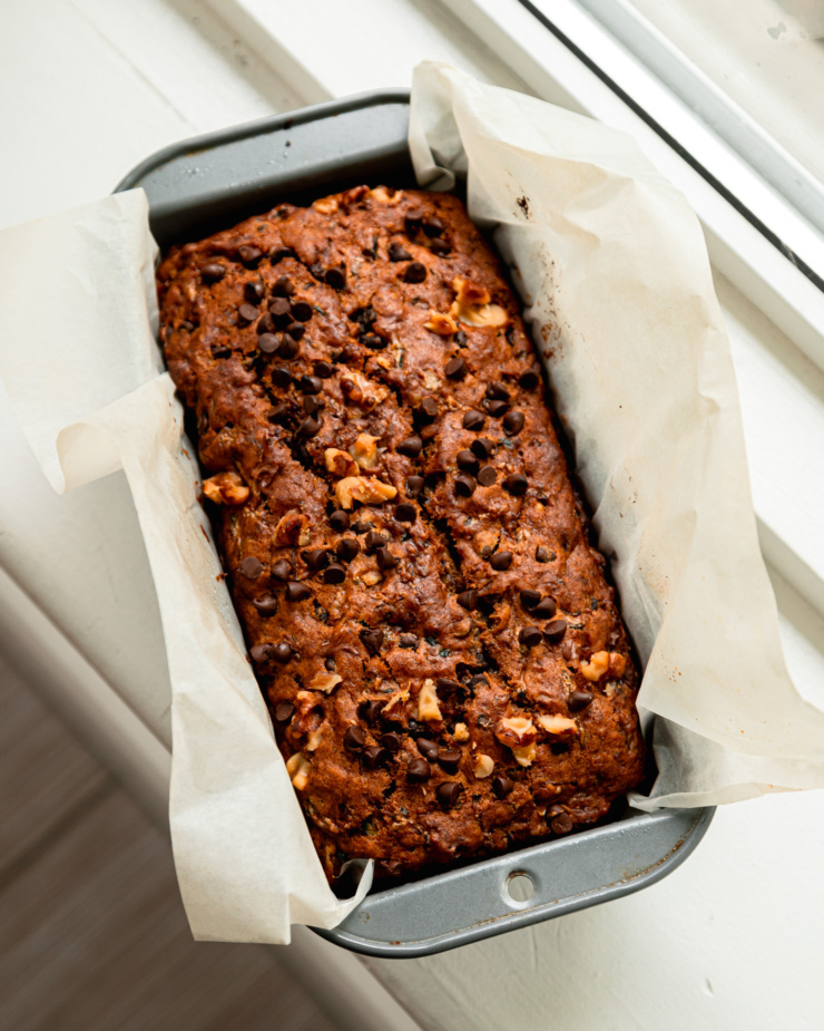 An overhead shot shows a freshly baked vegan zucchini bread topped with chocolate chips and chopped walnuts.
