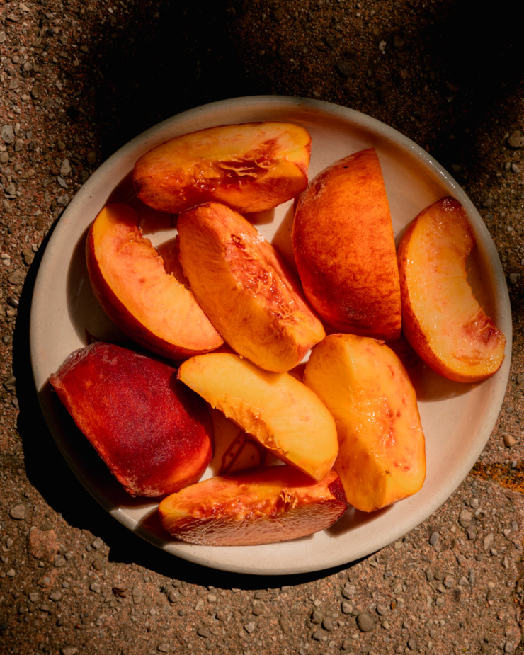 An overhead shot shows a plate of sliced peaches in the sun.
