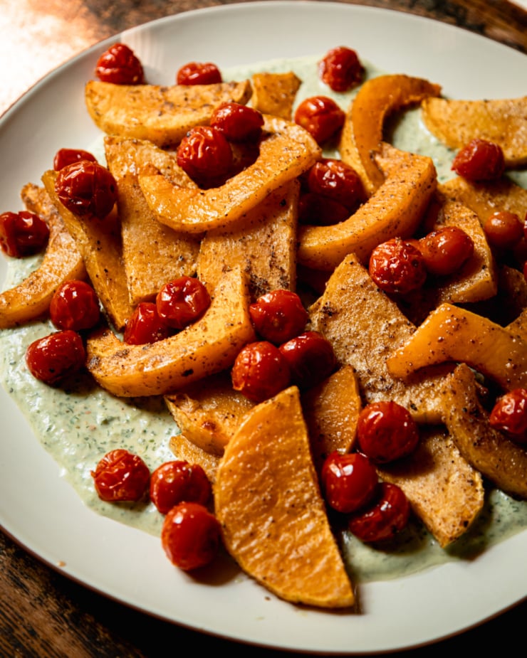 A 3/4 angle shot shows a platter piled high with roasted slices of butternut squash and burst cherry tomatoes.