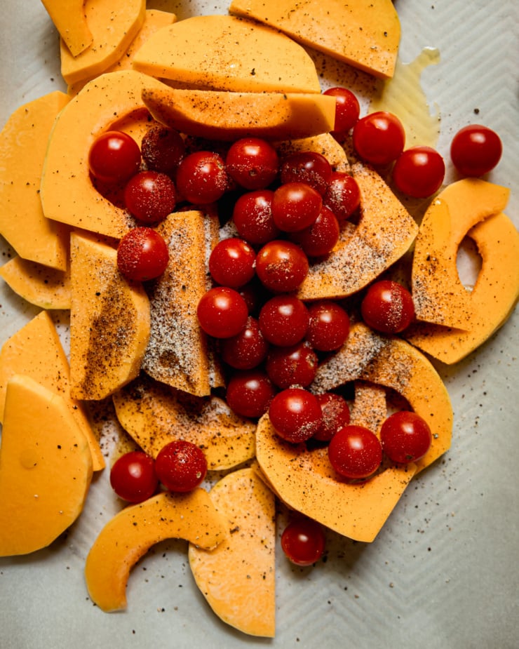 An overhead shot shows slices of butternut squash and cherry tomatoes on a parchment-lined baking sheet. The vegetables are dusted with spices and drizzled with olive oil.