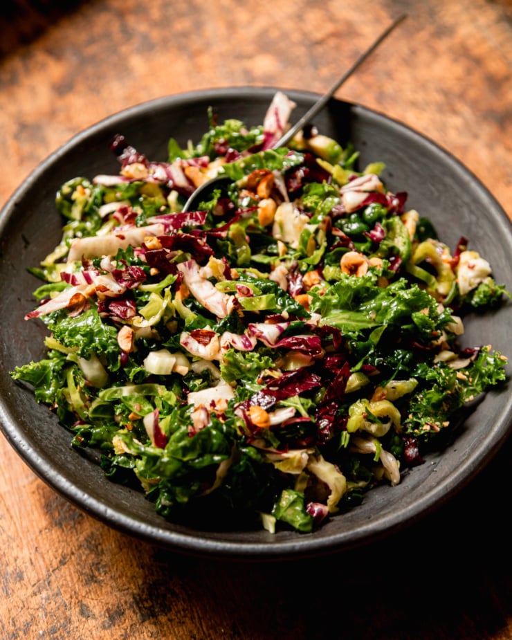 A 3/4 angle image shows an individual serving of a shredded fall greens salad topped with chopped hazelnuts.