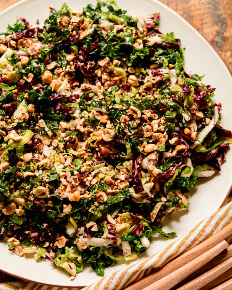 An overhead shot shows a shredded fall greens salad with sherry thyme vinaigrette and chopped hazelnuts. The greens are: kale, brussels sprouts and radicchio.