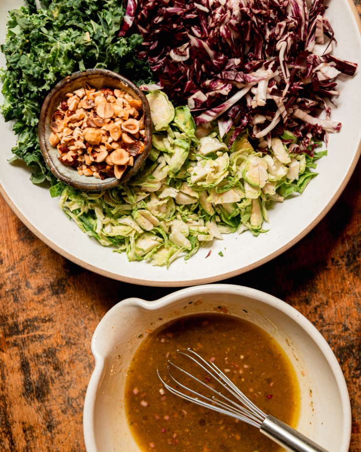 An overhead shot shows all the prepped components of a shredded fall greens salad with hazelnuts and sherry thyme vinaigrette.
