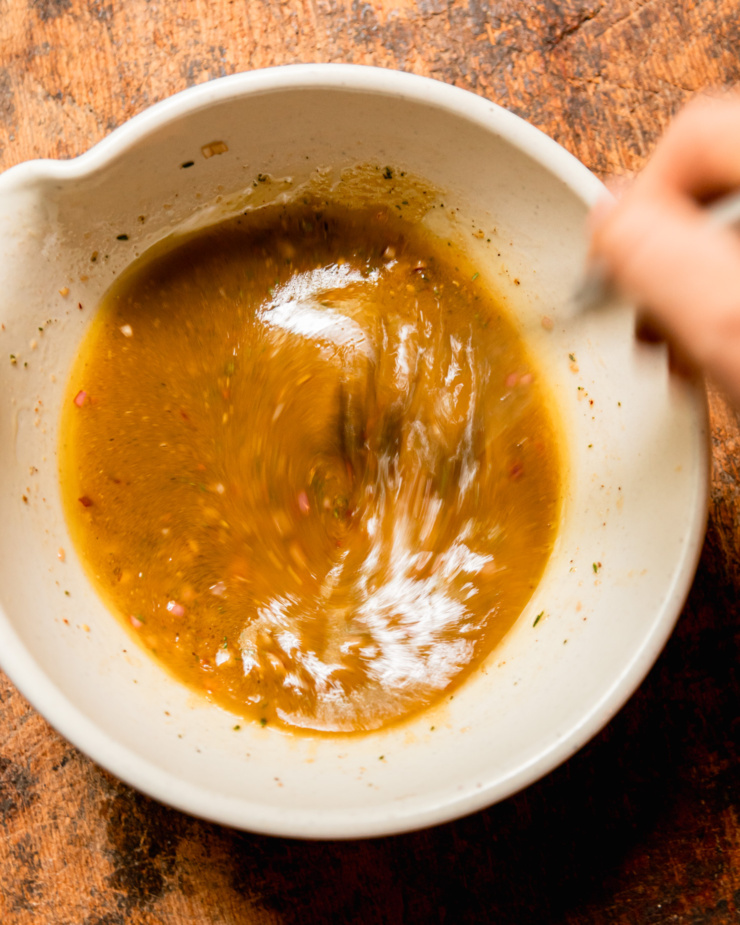 An overhead shot shows a hand using a whisk to bring a vinaigrette together in a bowl