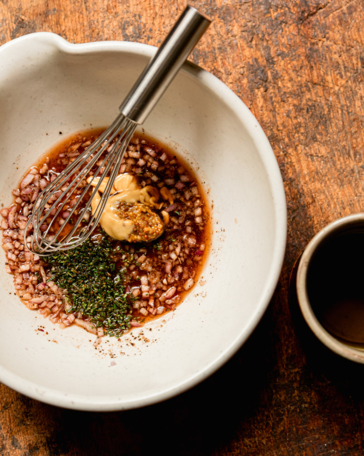 An overhead shot shows a bowl with a whisk and the base of a sherry thyme vinaigrette with two types of mustard and shallots.