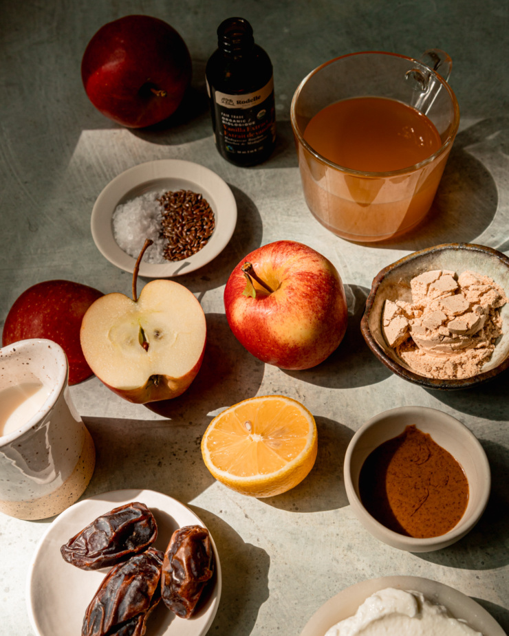 An overhead shot shows ingredients needed for a vegan salted caramel apple smoothie in bright, warm sunlight.
