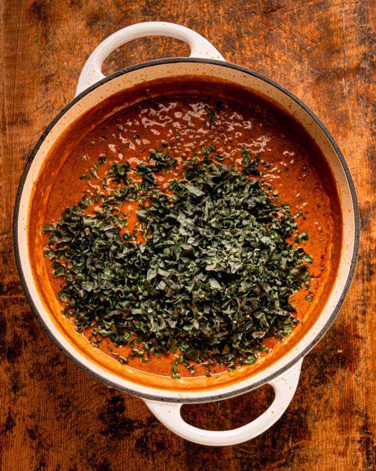 An overhead shot shows finely chopped kale on top of a creamy stew mixture in a braiser-style pot.