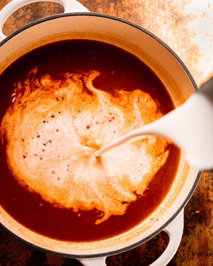 An overhead shot shows coconut milk being poured into a pot with a reddish brown liquid.