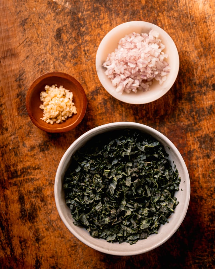 An overhead shot shows the following ingredients in prep bowls: finely chopped shallots, finely chopped kale, minced garlic.