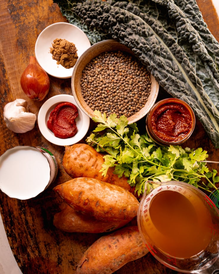 An overhead shot shows ingredients needed for a harissa coconut lentils dish with kale and roasted sweet potatoes.