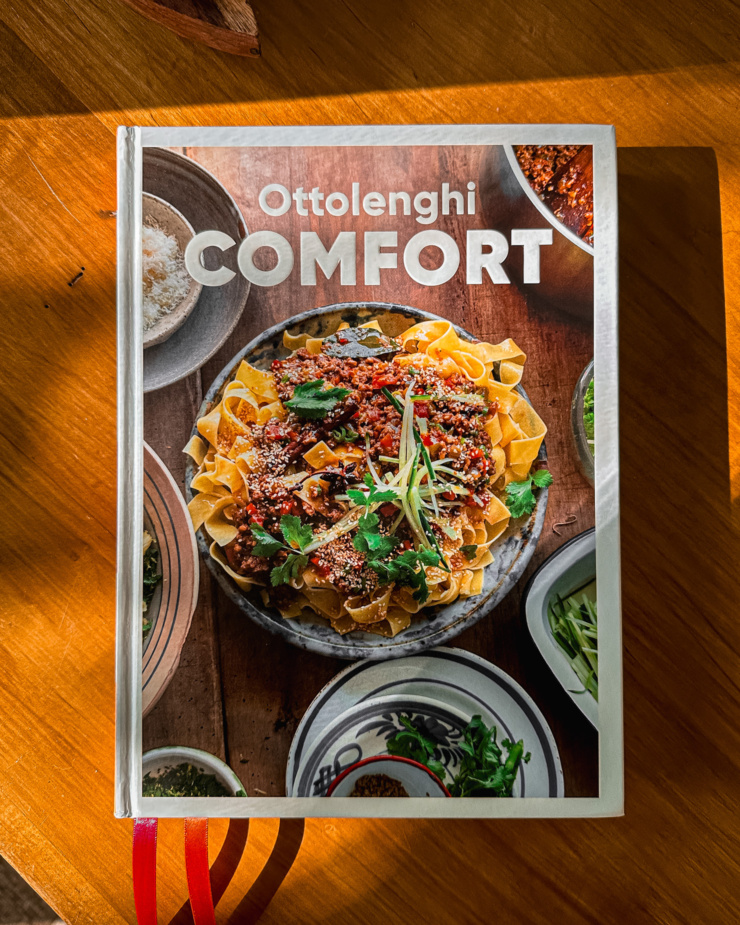 An overhead shot shows a copy of the cookbook "Ottolenghi Comfort" in a beam of sunlight.