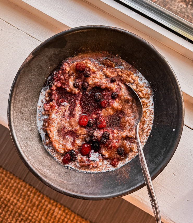 An overhead shot shows a bowl of steel cut oat porridge with blueberries, cranberries and cinnamon.