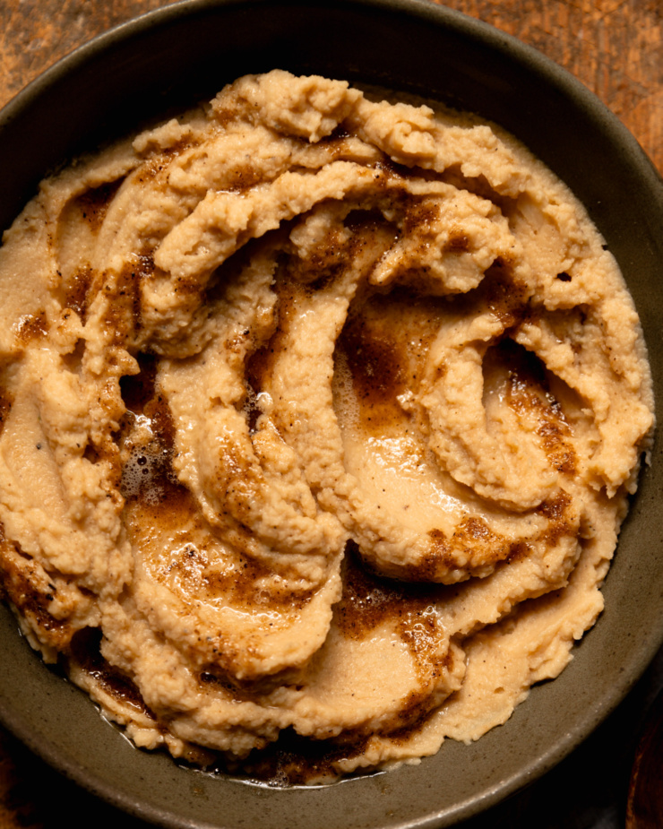 An overhead shot shows a bowl of mashed cauliflower with swoops of vegan Worcestershire black pepper butter on top.