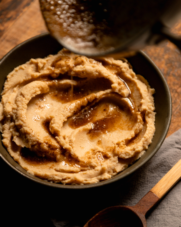 A 3/4 angle image shows melted Worcestershire black pepper butter being drizzled over mashed cauliflower in a serving bowl.