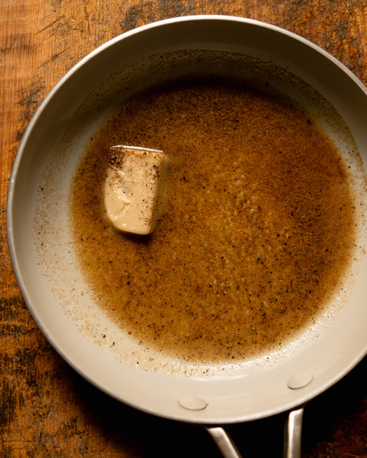 An overhead shot shows a small skillet with a pat of vegan butter, black pepper, and vegan Worcestershire sauce.