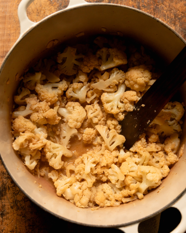 An overhead shot shows cooked cauliflower florets in a dutch oven pot.