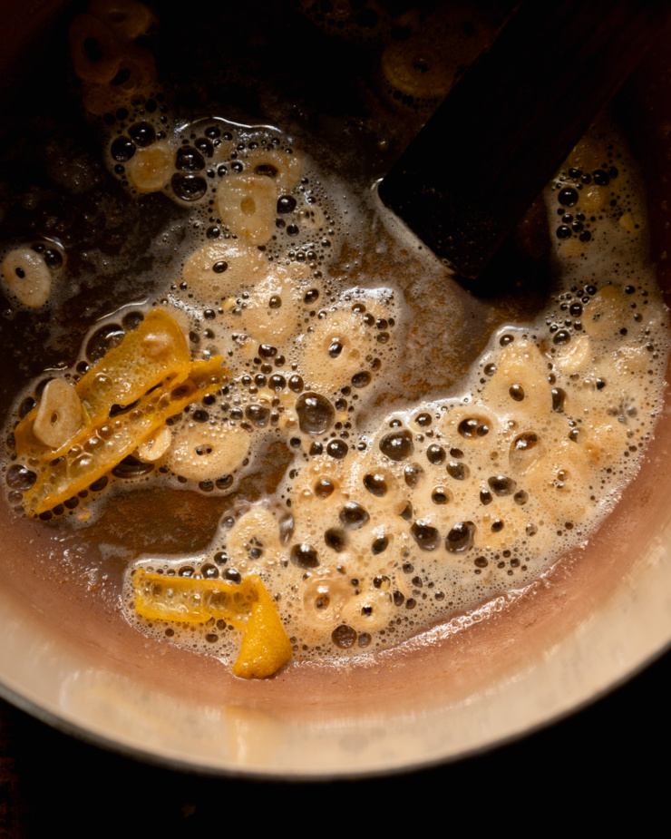 An up close, overhead shot shows lsiced garlic and lemon peels sizzling in vegan butter in a pot.