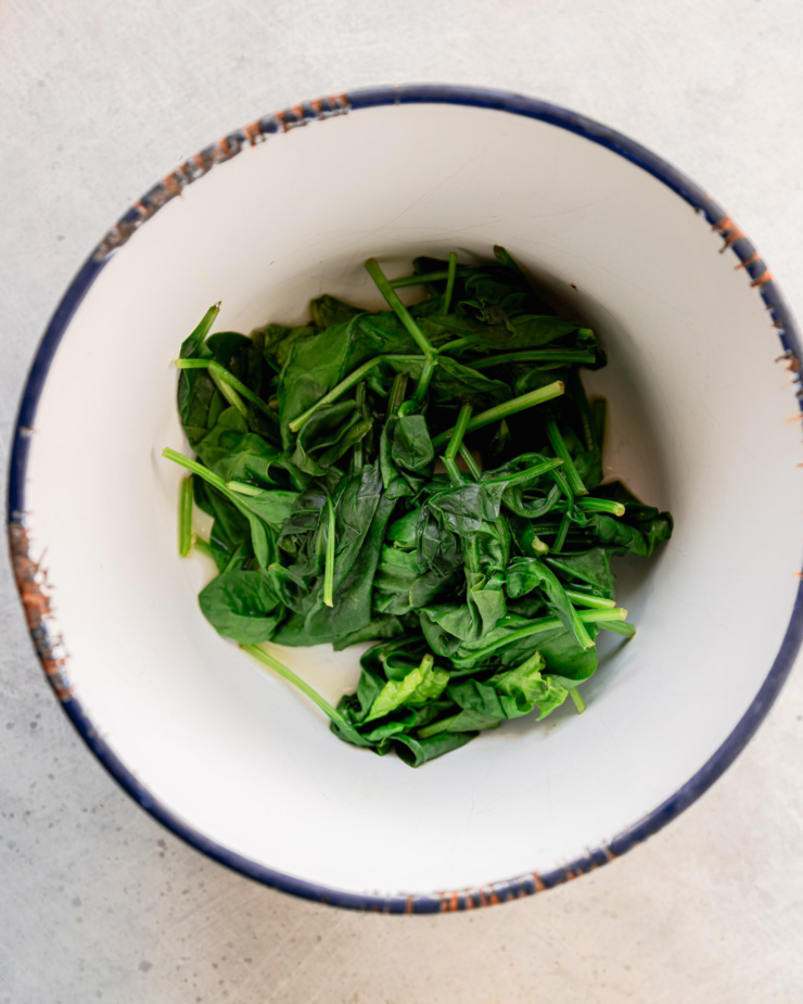 An overhead shot shows wilted spinach in a bowl.