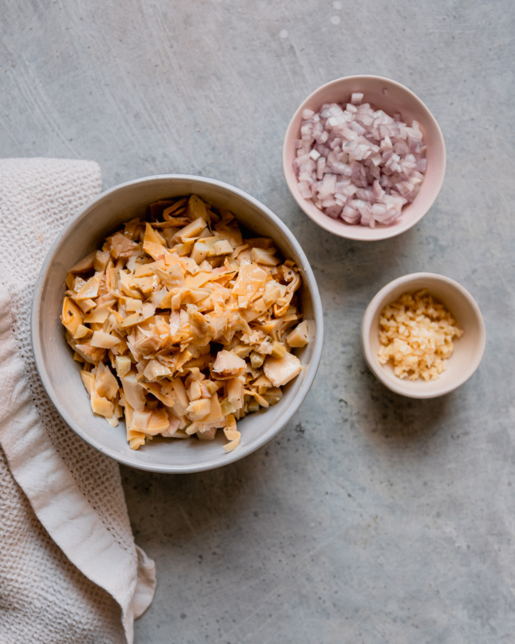 An overhead shot shows 3 bowls containing the following: chopped jarred artichokes, diced shallots, and minced garlic.