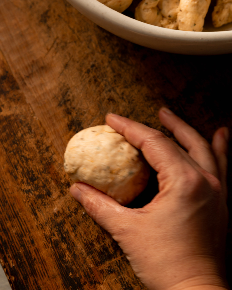 A 3/4 angle shot is blurry, showing the rolling motion of a hand bringing a ball of dough together.