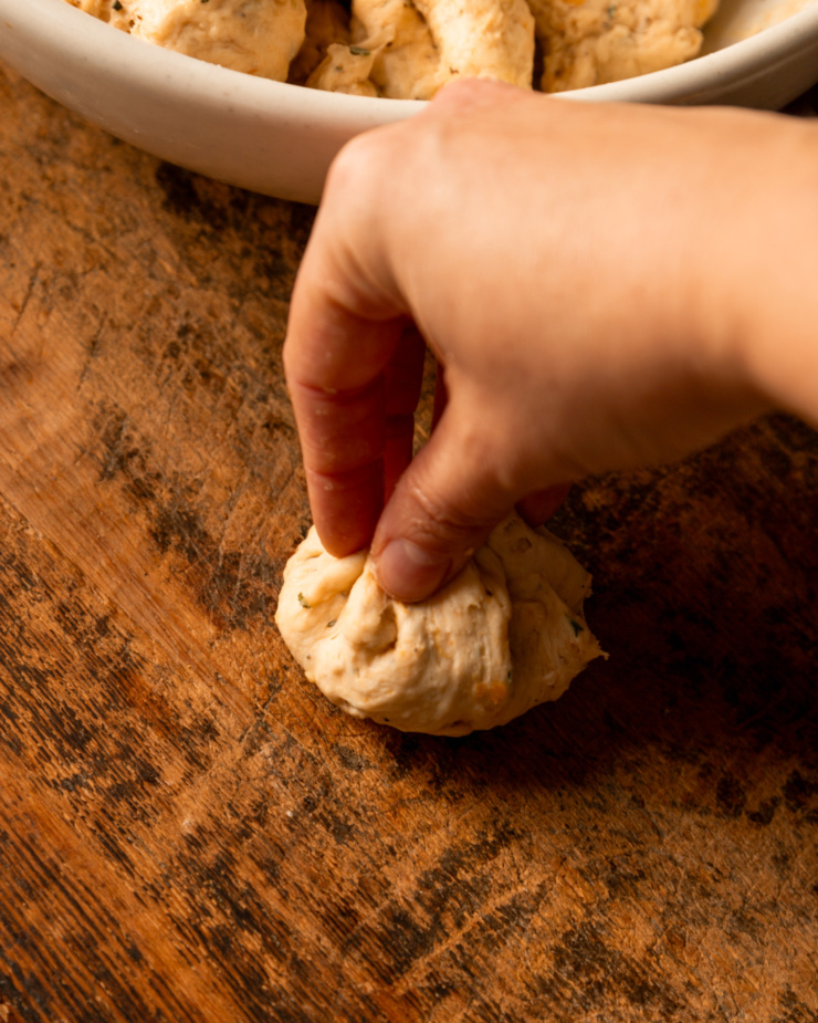 A 3/4 angle shot shows a hand pinching the edges of a portion of dough together, forming a ball.