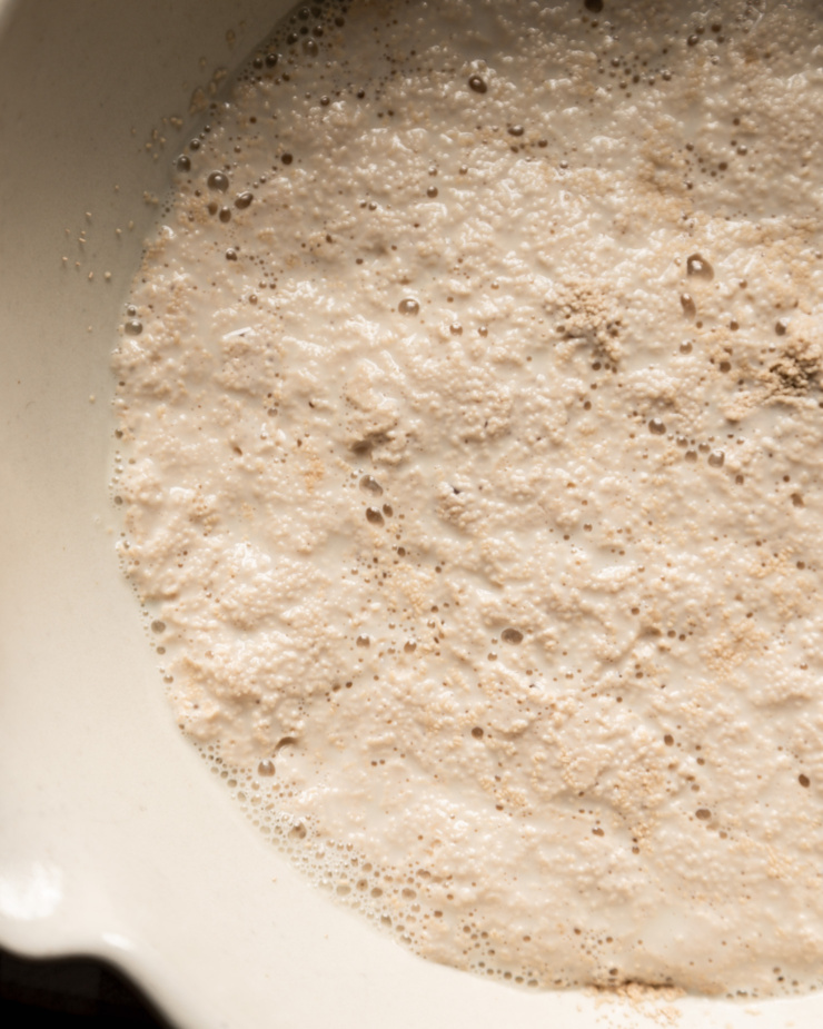 An overhead shot shows foamy activated yeast in a bowl of warm soy milk.