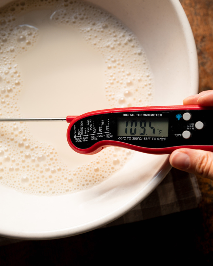 An overhead shot shows a thermometer in a bowl of warm soy milk reading 109 degrees Fahrenheit.