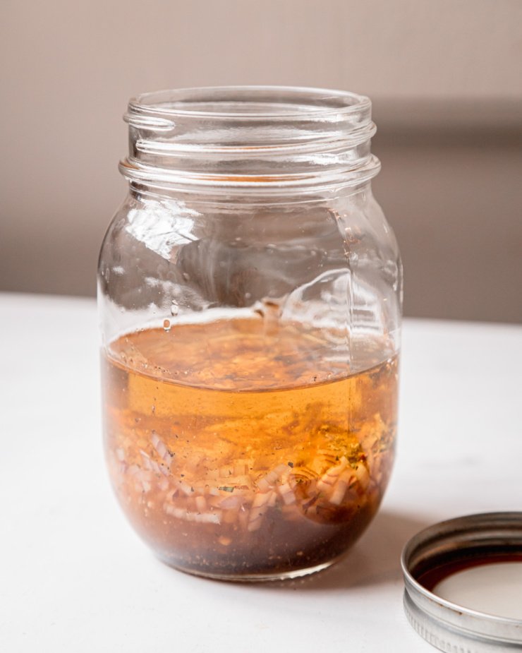 A head-on shot shows a salad dressing with shallots and white balsamic vinegar in a clear mason jar.