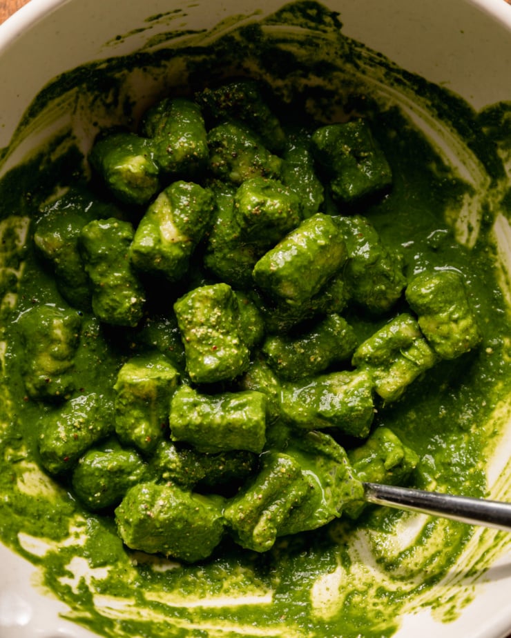An up close, overhead shot shows homemade gnocchi tossed in a deep green sauce in a bowl.