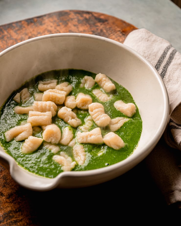 A 3/4 angle shot shows freshly drained gnocchi in a bowl with a thick green kale sauce.