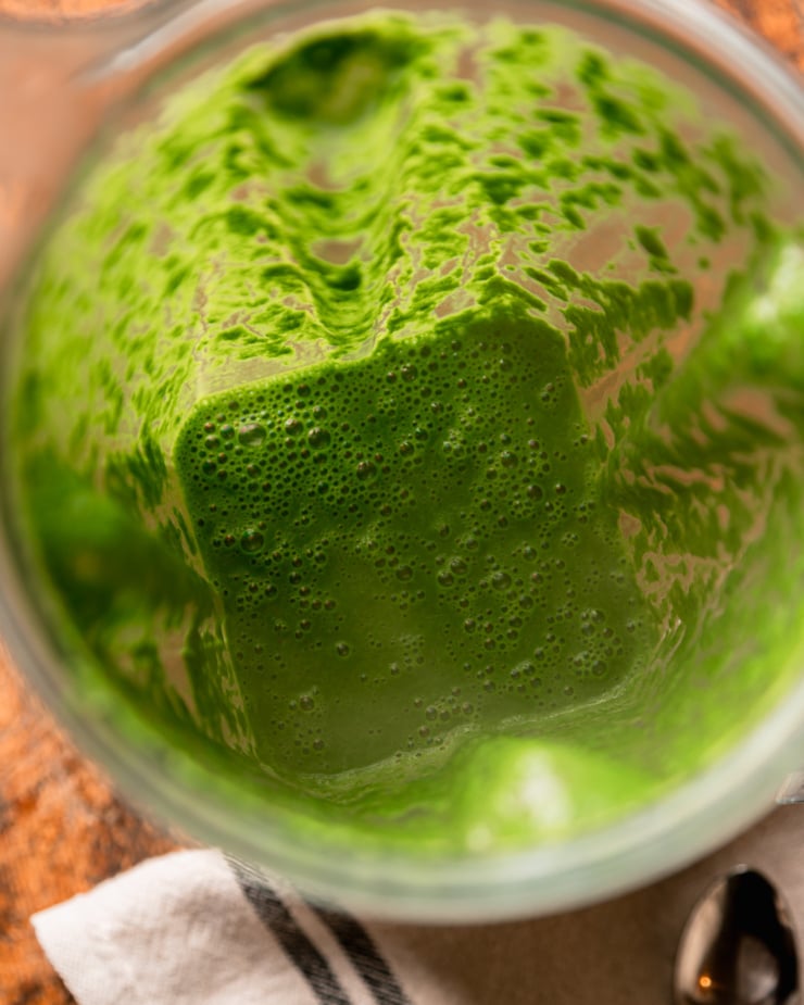 An overhead shot shows a thick green kale sauce in a blender pitcher.