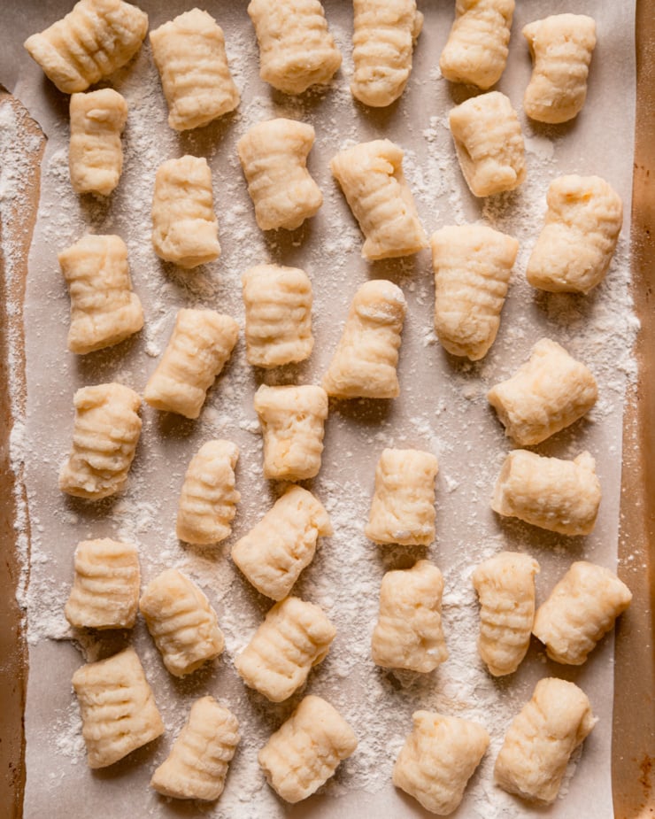 An overhead shot shows a bunch of freshly made vegan potato gnocchi on a parchment-lined baking sheet.
