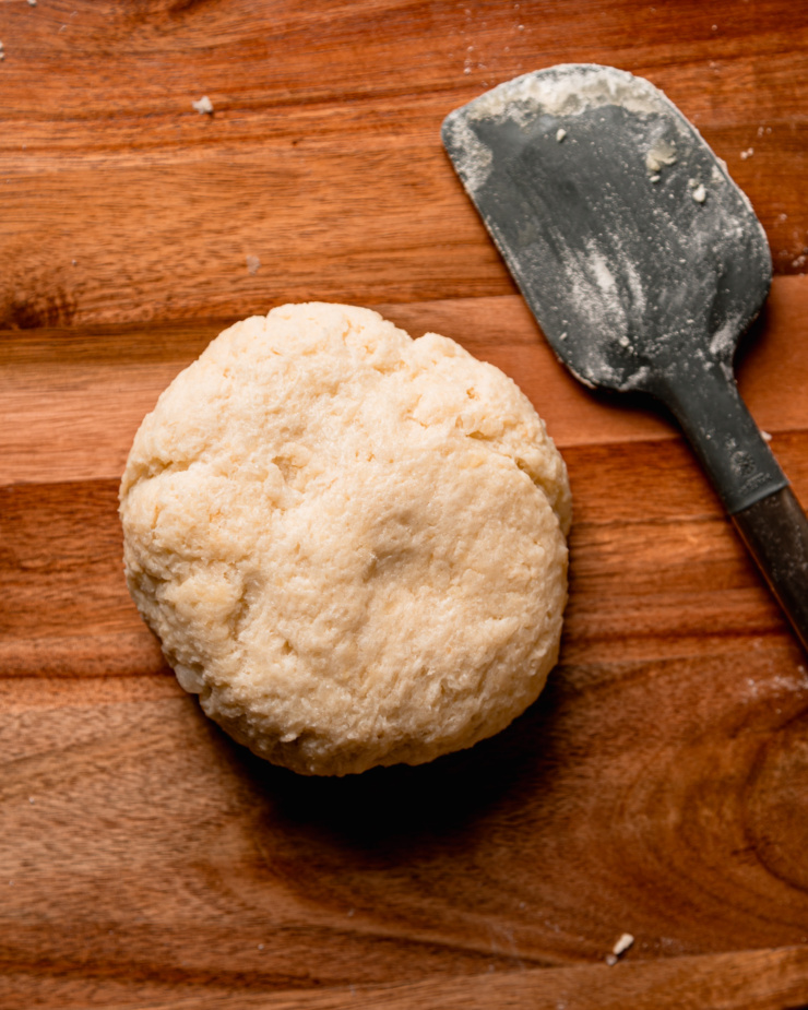 An overhead shot shows a ball of dough on a cutting board next to a spatula.