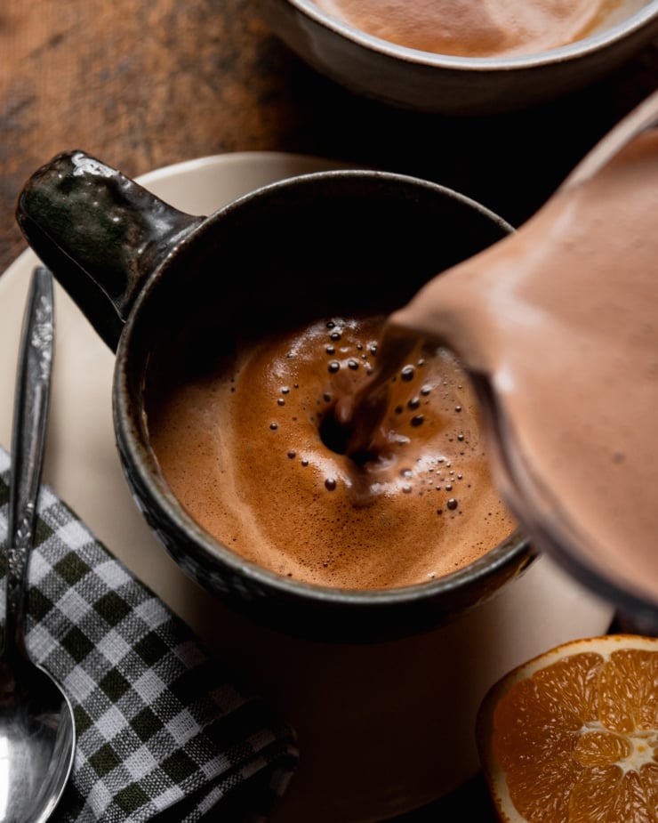 An overhead shot shows a chocolaty milk mixture being poured into a mug with espresso.